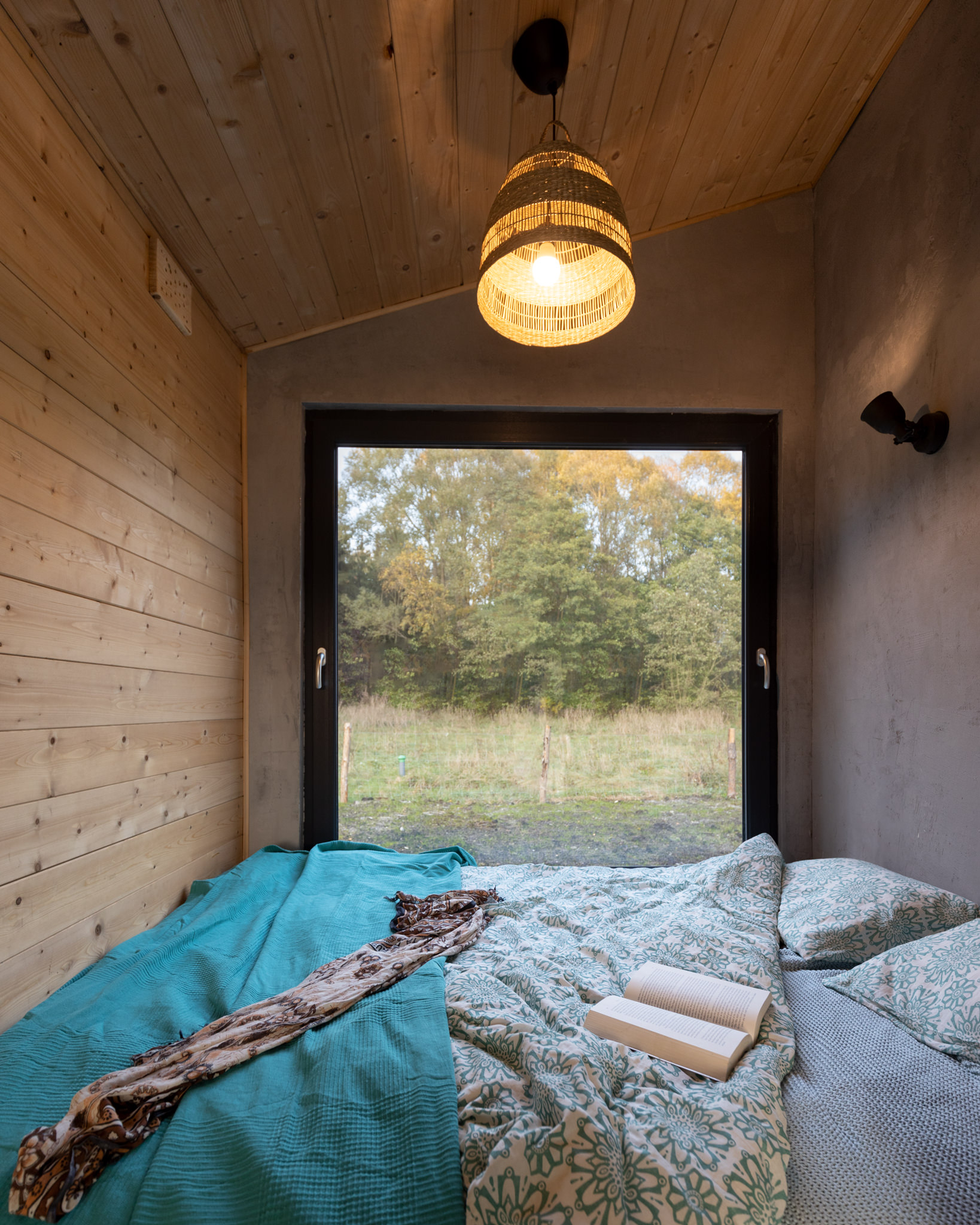 Sypialnia domku nad jeziorem z dużym oknem z widokiem na las