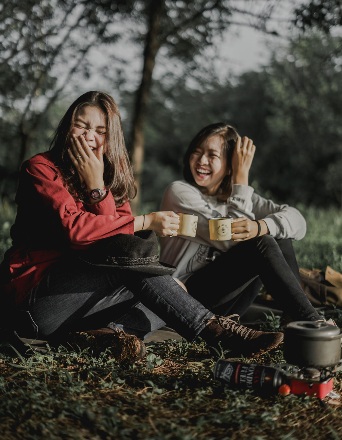 Śmiejące się kobiety siedzą na trawie w lesie i piją herbatę podgrzaną na gazie